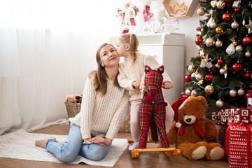 Girl kissing her mother at home near Christmas tree and gift boxes