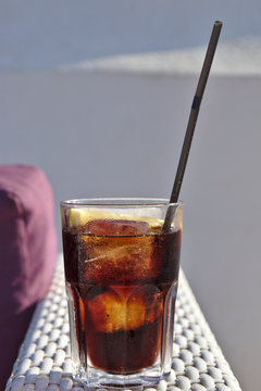 Glass of Cola with a slice of lemon, plastic straw and ice cubes