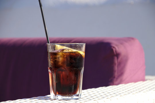 glass of cola on a table outside with a slice of lemon and a straw