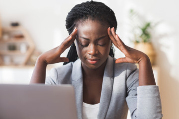Afro businesswoman massaging temple, trying to concentrate on work