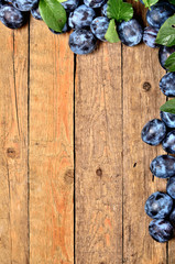 Fresh garden blue plums and leaves on rustic wooden background. VIew from above and copy space.