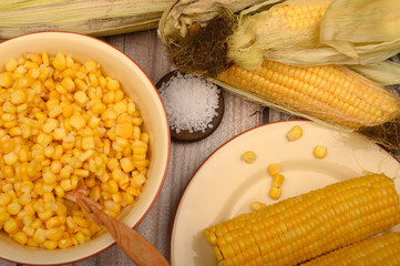 Grains of sweet corn in a plate with a wooden spoon, coarse salt and ears of corn on the table. Healthy diet. Fitness diet. For a sweet treat. Close up.