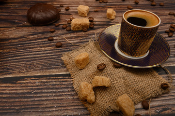 A Cup of coffee, pieces of brown sugar, marshmallows in chocolate and coffee beans on a wooden background. Close up.