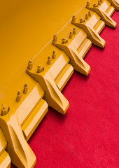 The metal part of the excavator bucket is shot close up on a red carpet background.