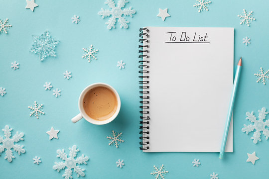 Cup of coffee, decorative snowflakes and notebook with to do list on turquoise background top view, Christmas and winter planning concept. Flat lay.
