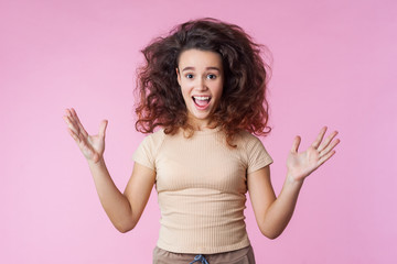 Portrait of crazy enthusiastic teenage girl with disheveled curly brunette hair flying up and in...