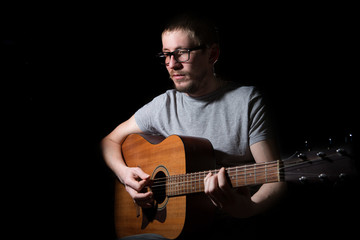 Obraz premium Young man playing on acoustic guitar on dark background