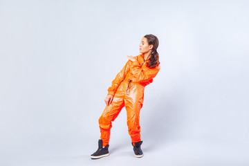 Full length image of talented teenage girl with brunette hair wearing bright orange jumpsuit dancing, showing hip hop move, youth hobby activities. indoor studio shot isolated on white background