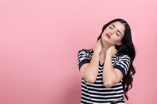 Young woman suffering from neck pain on a pink background