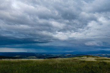 A meadow on top of a hill under a stormy sky