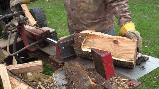 A man using a hydraulic log splitter to make firewood for the winter.