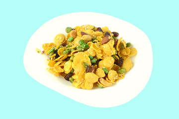 Cornflakes with dried fruits and nuts in white ceramic plate isolated on light blue background.