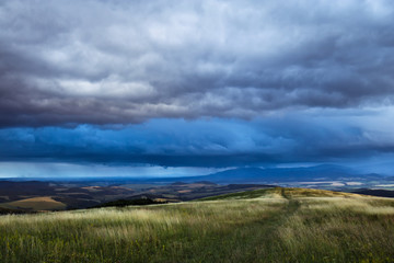 A grassy meadow with a road and a view under a stormy sky