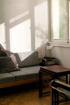 Empty room - interior in afternoon sunlight shining trough blinds, sofa, table and chair in corner by the window 