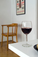 Glass of red wine on white table, blurred background with wooden chair in the corner, domestic interior