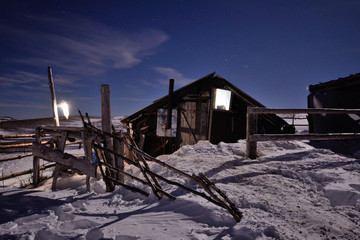 Small wooden shelter with lights inside, in the moonlight at winter night among snows, Caucasus...