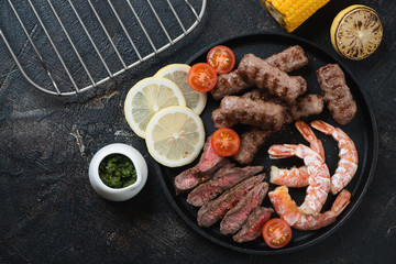 Surf and turf with beef meat, marbled beef sausages and shrimps, top view over dark brown stone background