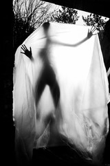 Slender nude girl, covered by a cellophane film, through which only her silhouette is visible and her nakedness is covered, in the ruins of a destroyed building. Conceptual, artistic, creative design.