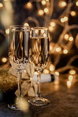 two champagne flute with shiny bottle on dark background with lights