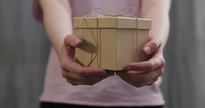 Slow motion young woman stand and show brown gift box with twine bow