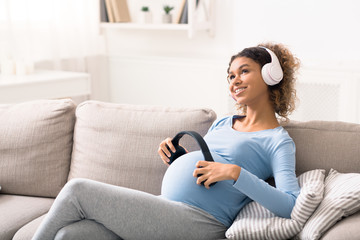 African-american pregnant woman listening to music in lving room - Powered by Adobe