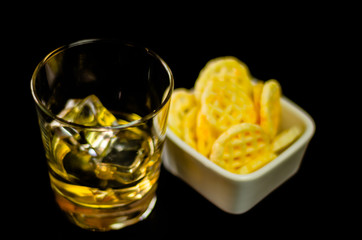 glass of whiskey with ice cubes and salty snacks on the background of the bar