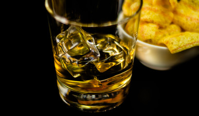 glass of whiskey with ice cubes and salty snacks on the background of the bar