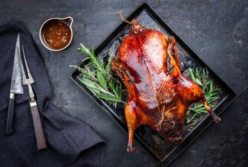 Traditional roasted stuffed Christmas Peking duck with herbs and sauce as top view on a rustic board