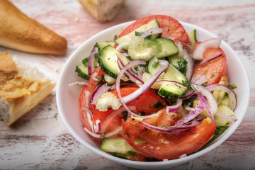 Still life food on a bright colorful background a white plate with a salad of cucumbers tomatoes onions sunflower oil and herbs and a French baguette