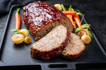 Traditional American meatloaf with ketchup from ground beef with carrots and onion as closeup modern design cast iron tray