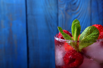 Red beverage with ice cubes, raspberries, strawberries and mint against the blue wooden background