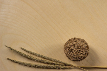 Three ears on a wooden background next to a ball of natural color threads. Three ears of wheat lie...