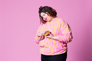 Sad plus size model with doughnuts, fat woman sadness and overeats on pink background