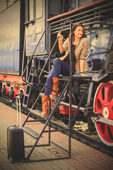 pretty middle-aged woman with luggage near the old steam locomotive