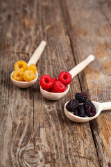 Ripe red and yellow raspberries and blackberries in spoons