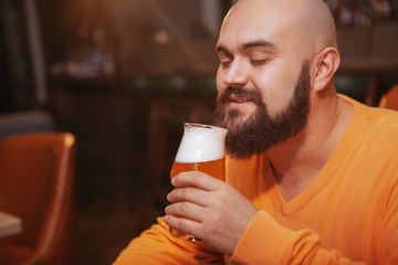 Close up of a cheerful bearded man smiling, smelling aroma of delicious beer in a glass