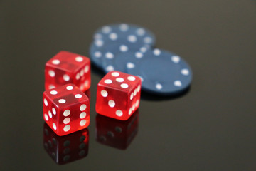 Red dice and casino gaming chips on dark mirrored table. Background for casino games, gambling, luck or randomness