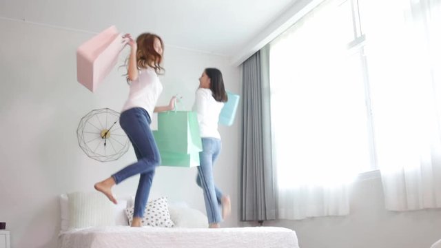 Asian pretty young woman jump on bed and holding  pastel shopping bag. She smiling and  happy shopping bags. she nice-looking lovely attractive shine and funny.