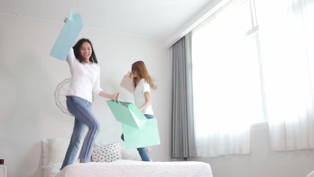 Asian pretty young woman jump on bed and holding  pastel shopping bag. She smiling and  happy shopping bags. she nice-looking lovely attractive shine and funny.