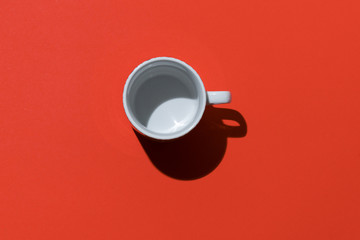 Empty tea cup on red paper background. Coffee mug from above. Minimal concept Hard deep shadow. Flat lay, top view.