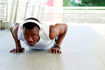 Portrait of a dark-skinned man wearing headphones to exercise by pushing up. - obrazy, fototapety, plakaty