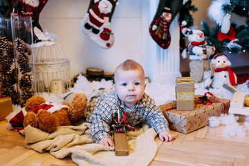 Little boy playing with Christmas gifts near New Year tree