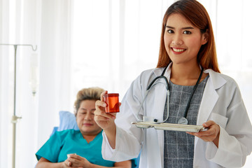 Portrait of a beautiful female doctor Smile and show the medicine bottle in hand With the backdrop of a sick person sleeping