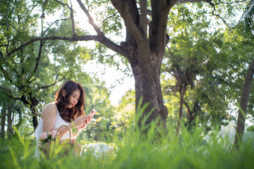 Fototapeta na wymiar Beautiful asian women sitting in green tree park using smartphone
