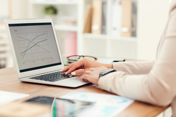 Side view close up of unrecognizable businesswoman analyzing statistics graphs while using laptop in office, copy space