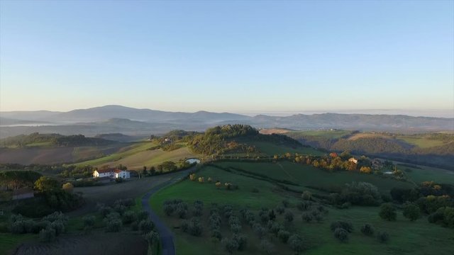 4k aerial drone rising flight footage at early morning grazing light over the green Tuscany countryside hills between Volterra and Cecina.