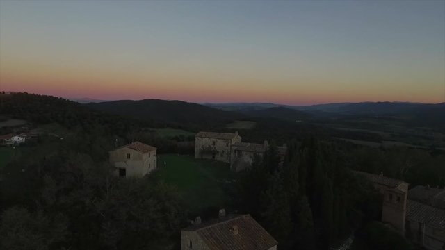 4k aerial  drone lowering flight footage at sunset time over the Tuscany countryside hills and the small ancien village of Gello near Volterra.