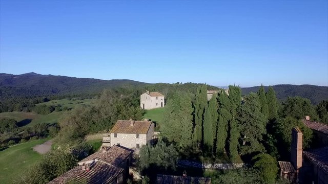 4k aerial  drone backward flight footage at midday time over the Tuscany countryside hills and the small ancien village of Gello near Volterra, Italy.