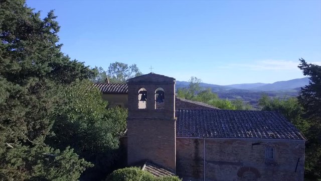 4k aerial  drone rising flight footage at midday time over the Tuscany countryside hills and the church of the small ancien village of Gello near Volterra, Italy.