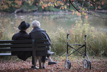 Senior couple man and woman are resting on a bench in the autumn park. Effect neutral and pastel color images.
